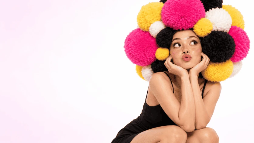 Personnage à la coiffure de pompons roses, jaunes et noirs sur fond clair